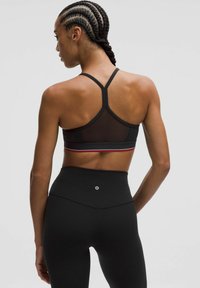 Sostén deportivo negro con panel de malla, diseño de espalda deportiva y sutiles rayas rojas y grises. Pantalones leggins negros de cintura alta con detalle de logo.