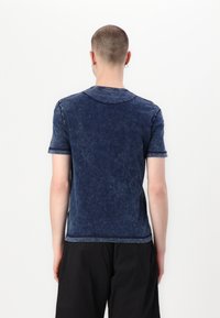 Tricou din bumbac de culoare bleumarin, cu mâneci scurte, textură decolorată, guler rotund și detalii de cusătură vizibile la umeri și la tiv.