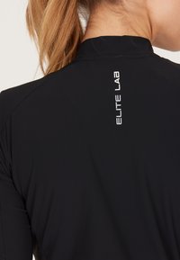 Svart sporttröja med hög krage och strukturerad tyg. På baksidan finns texten "ELITE LAB" i vitt.