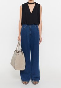Top negro sin mangas con un escote en V profundo, combinado con jeans de mezclilla azul de pierna ancha. Bolsa gris claro con herrajes plateados y sandalias con bordes deshilachados.