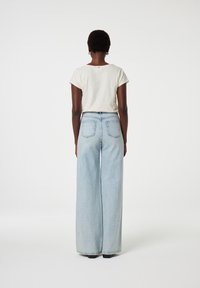 Losjes zittende lichtblauwe denim broeken met een hoge taille, voorzien van twee achterzakken en een zacht beige T-shirt met korte mouwen en gestikte accenten.
