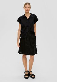 Chemise noire en lin à manches courtes avec un devant boutonné, associée à une jupe noire en coupe A dotée d'une taille élastique et de poches latérales.