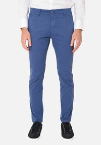 Chinos in cotone blu con una vestibilità slim, dotati di passanti per la cintura, chiusura con bottone e tasche laterali. Indossati con sneakers nere con lacci.