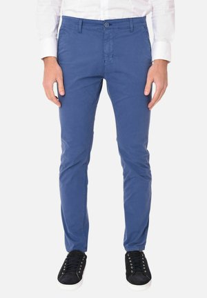 Chinos in cotone blu con una vestibilità slim, dotati di passanti per la cintura, chiusura con bottone e tasche laterali. Indossati con sneakers nere con lacci.
