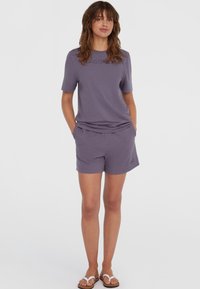 Lilla bomulds t-shirt med korte ærmer og logo, parret med matchende shorts med elastisk talje og sidelommer. Flip-flops fuldender looket.