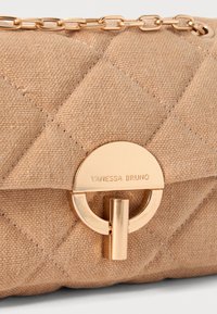 Borsa in tessuto trapuntato beige chiaro con clasp circolare dorato e tracolla a catena. Il nome del marchio "VANESSA BRUNO" è impresso sul clasp.