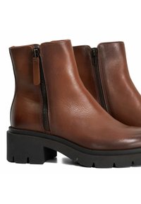 Brown leather ankle boots with a slightly glossy finish, featuring dual side zippers and chunky black rubber soles.