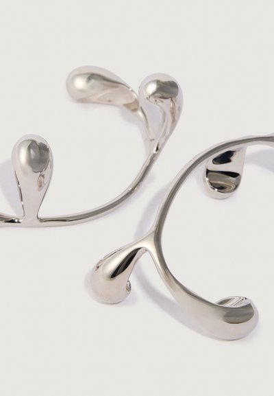 Due massaggiatori in argento lucidato con estremità arrotondate su una superficie bianca, progettati per un uso manuale e il sollievo muscolare.