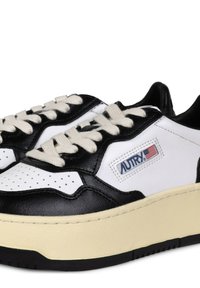 Sneakers in pelle bianca e nera con suola cremosa chunky, caratterizzati da dettagli perforati, lacci crema e un piccolo logo del marchio.