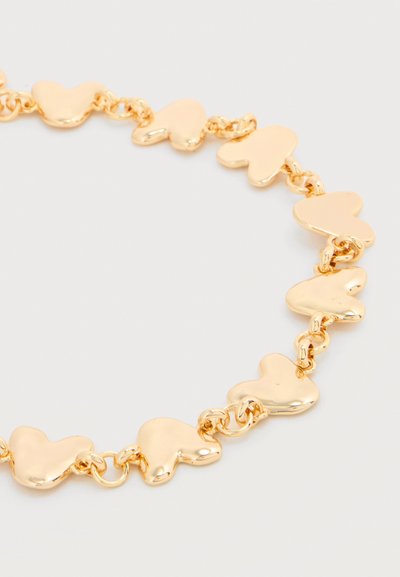 Βραχιόλι με αλυσίδα από χρυσό με συνδεδεμένους γυαλιστερούς κρίκους σε σχήμα καρδιάς σε φωτεινό φόντο.