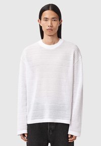 Hvid langærmet sweater med teksturerede vandrette striber, rund halsudskæring og sænkede skuldersømme. Stylet med mørke jeans.