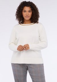 Weißer Pullover mit geripptem Saum und Bündchen, verziert mit einer goldenen Kettenakzent um den Halsausschnitt. Kombiniert mit karierten Hosen.