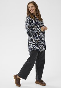 Langærmet skjorte med et navy, creme og orange abstrakt zebra mønster, parret med højtaljede sorte denim og brune chunky-sålede sko.