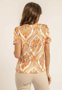 Blouse à manches courtes en tissu satiné avec un motif paisley complexe orange et vert sur un fond clair.