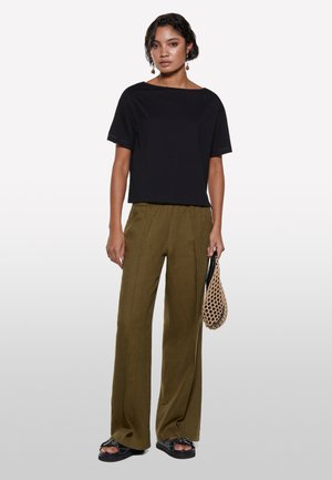 Top corto nero a maniche corte abbinato a pantaloni larghi verde oliva. Il modello tiene in mano una borsa di rete, indossando sandali neri con suola spessa.