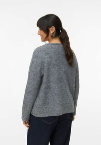 Suéter gris de punto con un acabado texturizado, escote redondo, hombros caídos y un corte relajado; se muestra combinado con jeans oscuros.