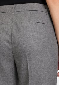 Pantalons en laine gris présentant un design élégant avec une texture lisse, des poches arrière plates et une coupe ajustée à la taille.