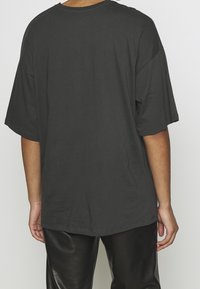Camiseta oversized gris oscuro con mangas cortas y cuello redondo, hecha de una tela suave, con un dobladillo recto. Llevada con pantalones negros brillantes.
