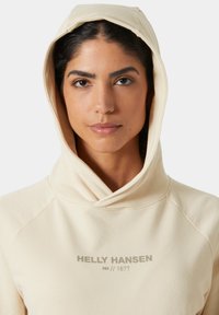 Beige hoodie met een zachte textuur, raglanmouwen en "HELly HANSEN // 1877" in lichtgrijs gedrukt op de borst.