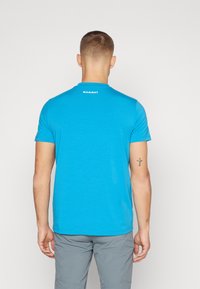 Camiseta de manga corta en color turquesa con cuello redondo, que presenta un logo blanco de "MAMMUT" en la parte posterior. Textura suave, corte casual.