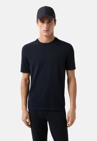 Marineblauer kurzärmliger Strickpullover mit Rundhalsausschnitt und gerippten Abschlüssen, kombiniert mit einer passenden marinen Mütze, die ein elegantes, minimalistisches Design präsentiert.