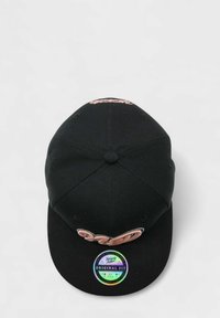 Mustapäällä baseball-lippis, jossa on etuosassa kirjailtu vaaleanpunainen teksti, litteä lippa ja kehykseen ommeltu värikäs tarra, jossa lukee "Alkuperäinen istuvuus."