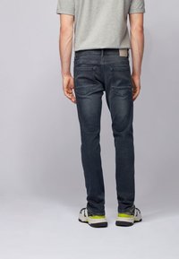 Granatowe dżinsy o slim fit, z dwiema tylkami kieszeniami i teksturowaną powierzchnią. Noszone z szarym t-shirtem i butami sportowymi.