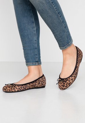 Person iført blå skinny jeans og leopardprintede ballerinaer med sort kant og sløjfe, stående på et hvidt gulv.