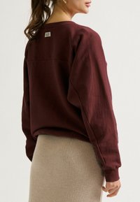 Bordeaux sweatshirt met een relaxte pasvorm, geribbelde manchetten en een gestikte achterkant. Gecombineerd met een zachte beige geribbelde rok.