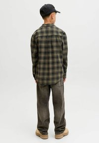 Rutet flannel skjorte i grøn og sort, med en rund kant, parret med falmede grå jeans og beige sko, set fra ryggen.