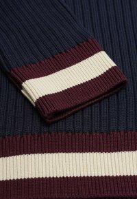 Stickad tröja med ribbad textur. Färgblockdesign med marinblå, vinröd och krämfärgade ränder vid ärmsluten och nederkanten.