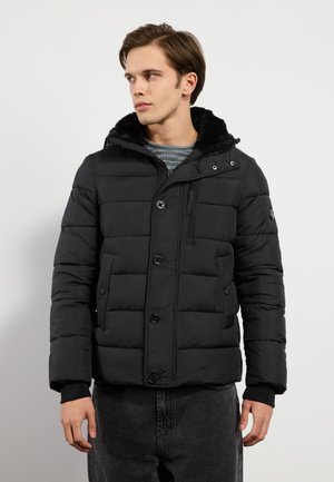 Chaqueta acolchada negra con cierre de botones en la parte delantera, capucha forrada de piel y puños acanalados. Presenta un diseño acolchado y bolsillos laterales.