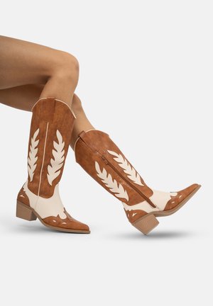 Botas de cuero vaqueras en tonos bronce y blanco con recortes en forma de hoja, secciones elevadas y tacón bajo tipo bloque; cierre lateral con cremallera.