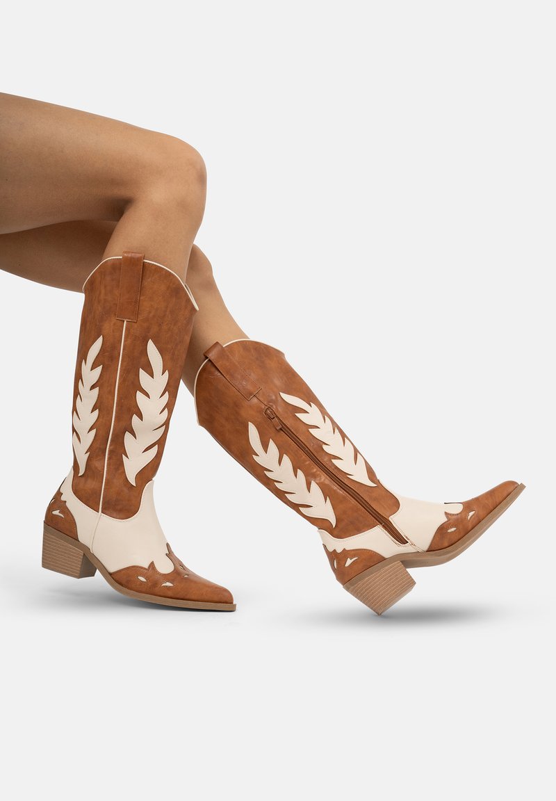 Botas de cuero vaqueras en tonos bronce y blanco con recortes en forma de hoja, secciones elevadas y tacón bajo tipo bloque; cierre lateral con cremallera.