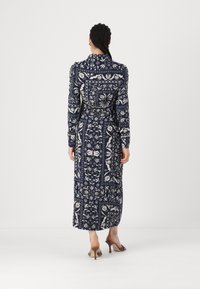 Abito lungo a maniche lunghe di colore blu navy con un motivo floreale e geometrico bianco, vita con cintura e orlo leggermente svasato.