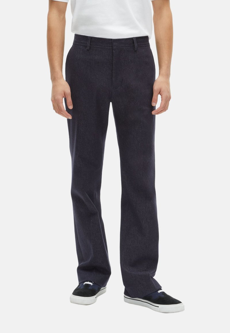 Donkerblauwe denim broek met een rechtlopende pasvorm, voorzien van voorzakken en een soepele textuur, gecombineerd met zwart-witte sneakers.