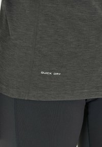 Dunkelgraues, schnell trocknendes Stoffhemdsaum über schwarzen Leggings, das die Textur des Stoffes und die Nähdetails zeigt.