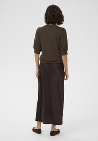 Brown pullover with short, puffed sleeves paired with a long, dark brown skirt. Soft texture, minimal design, and flat brown shoes accentuate the look.