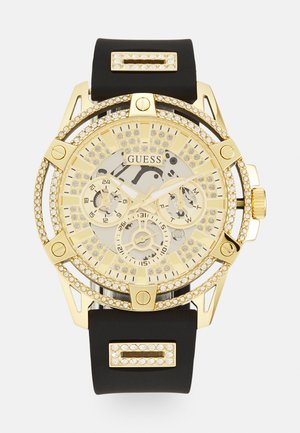 Montre-bracelet dorée avec accents en cristal, cadran transparent, bracelet en caoutchouc noir, et plusieurs sous-cadrans pour afficher l'heure et la date.