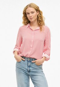 Blouse rayée rouge et blanche avec un devant à boutons, des manches retroussées et une coupe décontractée, associée à un jean bleu taille haute.