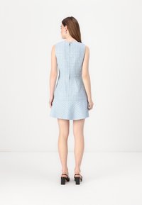 Robe sans manches bleu clair avec un motif texturé, corsage ajusté, jupe évasée et fermeture éclair au dos. Sandales à talons carrés noires.