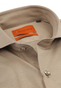 Beige katoenen shirt met een klassieke kraag, knoopsluiting en merklabels, met een soepele textuur en subtiele ribbeldetails.
