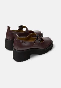 Scarpe Mary Jane in pelle bordeaux con un robusto tacco nero, caratterizzate da una larga fascia con fibbia e dettagli intagliati ai lati.