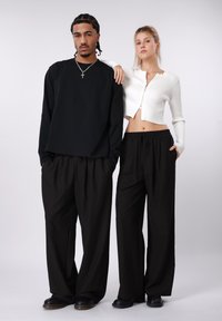 Sort langærmet skjorte, løstsiddende, stribede bukser i sort med røde accenter, hvid ribstrikket kort cardigan med lynlås foran.