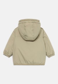 Doudoune beige avec capuche, poignets élastiqués et texture douce et mate. Présente une forme carrée et aucun système de fermeture visible.