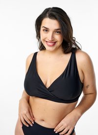 Črni bikini zgornji del z ovitkom, širokimi naramnicami in gladko teksturo, v kombinaciji s usklajenimi spodnjimi deli. Model se smeji in prikazuje prileganje.