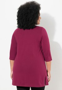 Tunika bordeaux con maniche tre quarti, spacchi laterali e una texture morbida e liscia. Progettata per un comfort ottimale e libertà di movimento.