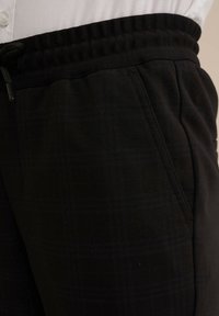 Pantaloni de jogging negri dintr-un material texturat, având un model discret în carouri. Talie elastică cu șnur și buzunare laterale.