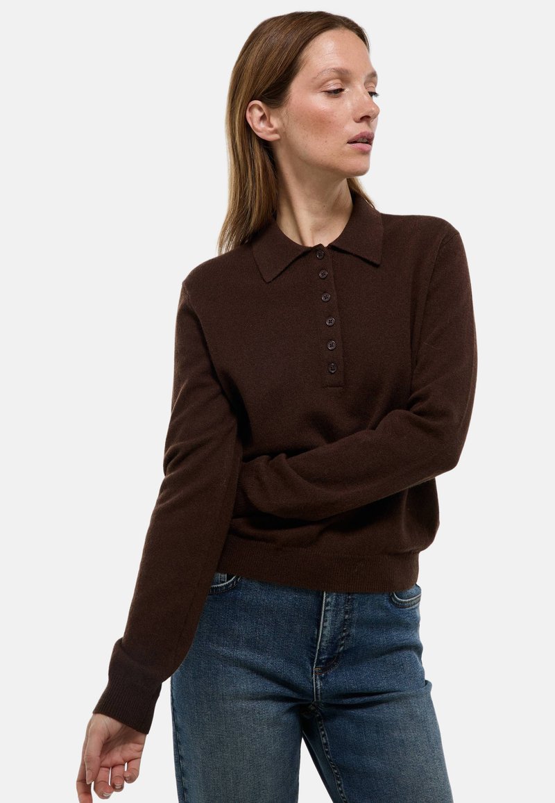 Pull en tricot marron avec un col et une patte de boutonnage à sept boutons. Manches longues avec des poignets côtelés. Porté avec un jean en denim bleu.