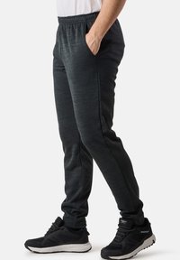Dunkelgraue Sport-Jogginghosen für Herren aus strukturiertem Stoff, mit elastischem Bund, seitlichen Taschen und schmal zulaufendem Bein, kombiniert mit schwarzen Laufschuhen.